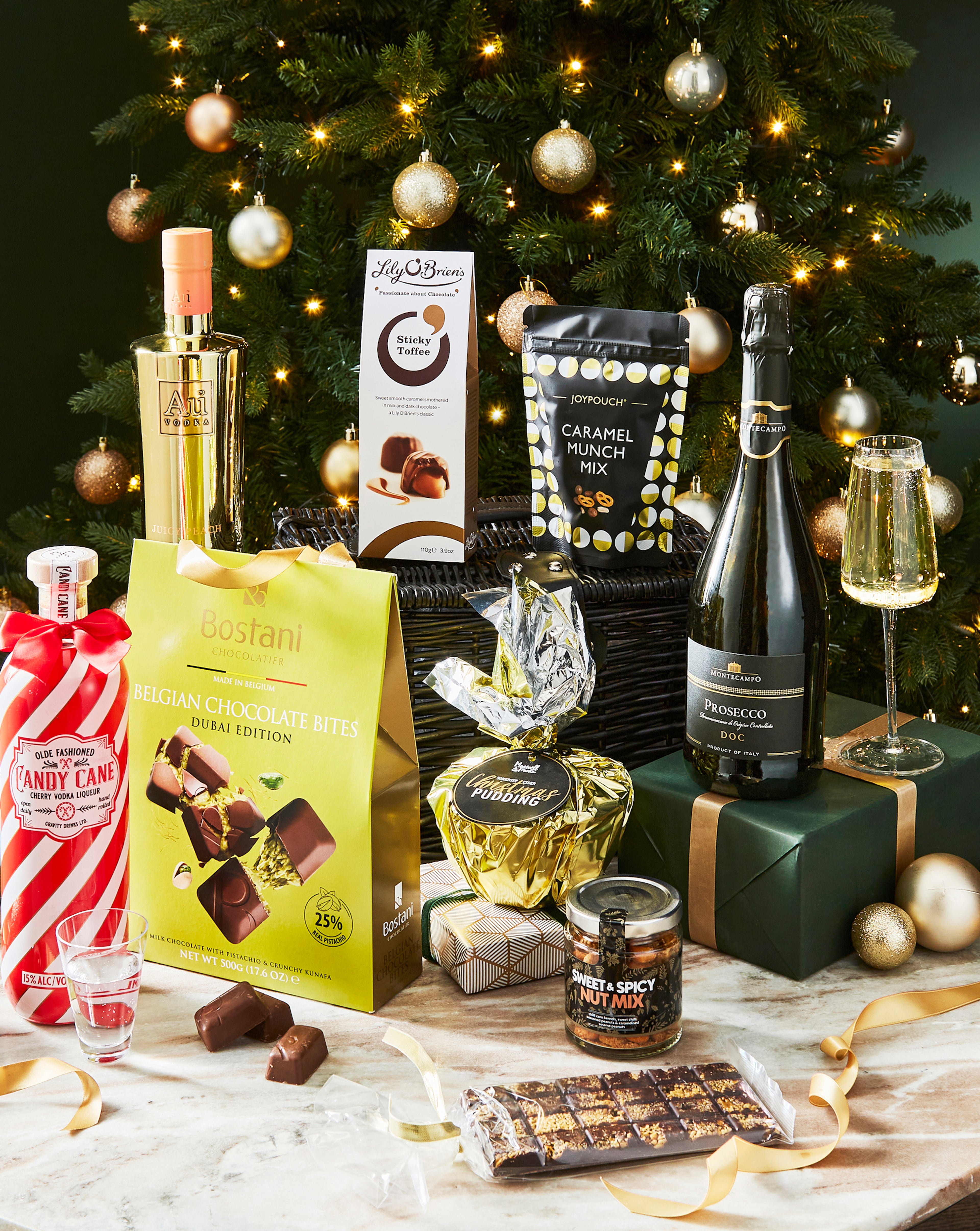 Festive display with a Christmas tree and assorted luxury treats, including chocolates, prosecco and snacks.