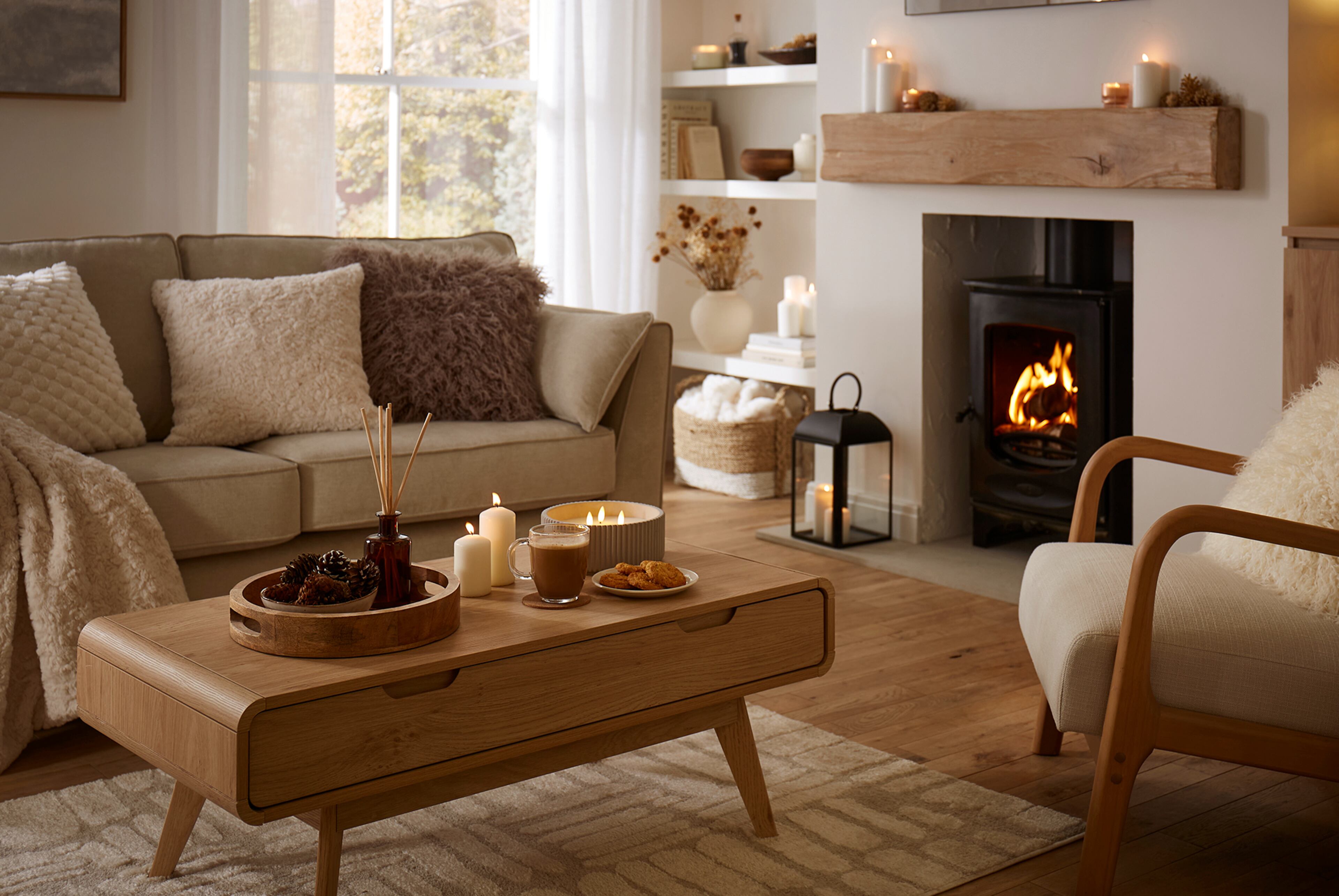 Cosy living room with a beige sofa, wooden coffee table with candles and drinks, and a lit fireplace.